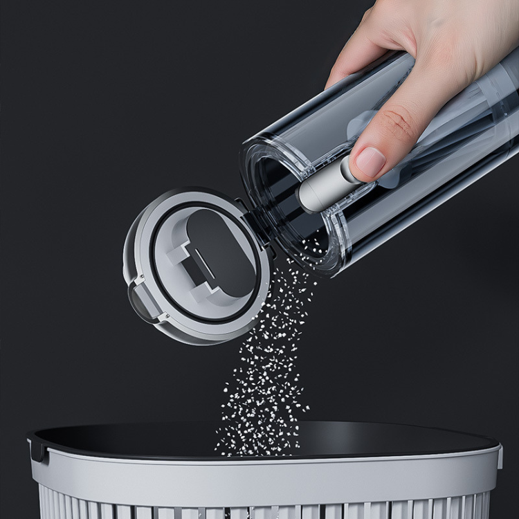 Hand pouring small particles from a container into a trash bin against a black background